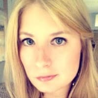 A woman with long blonde hair and blue eyes looks directly at the camera, with a soft-focus background.